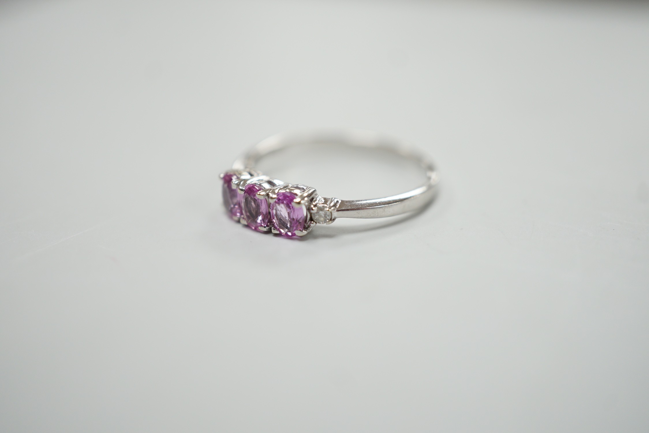 A modern 14ct white gold, three stone pink sapphire and two stone diamond chip set ring, size L, gross weight 1.5 grams.
